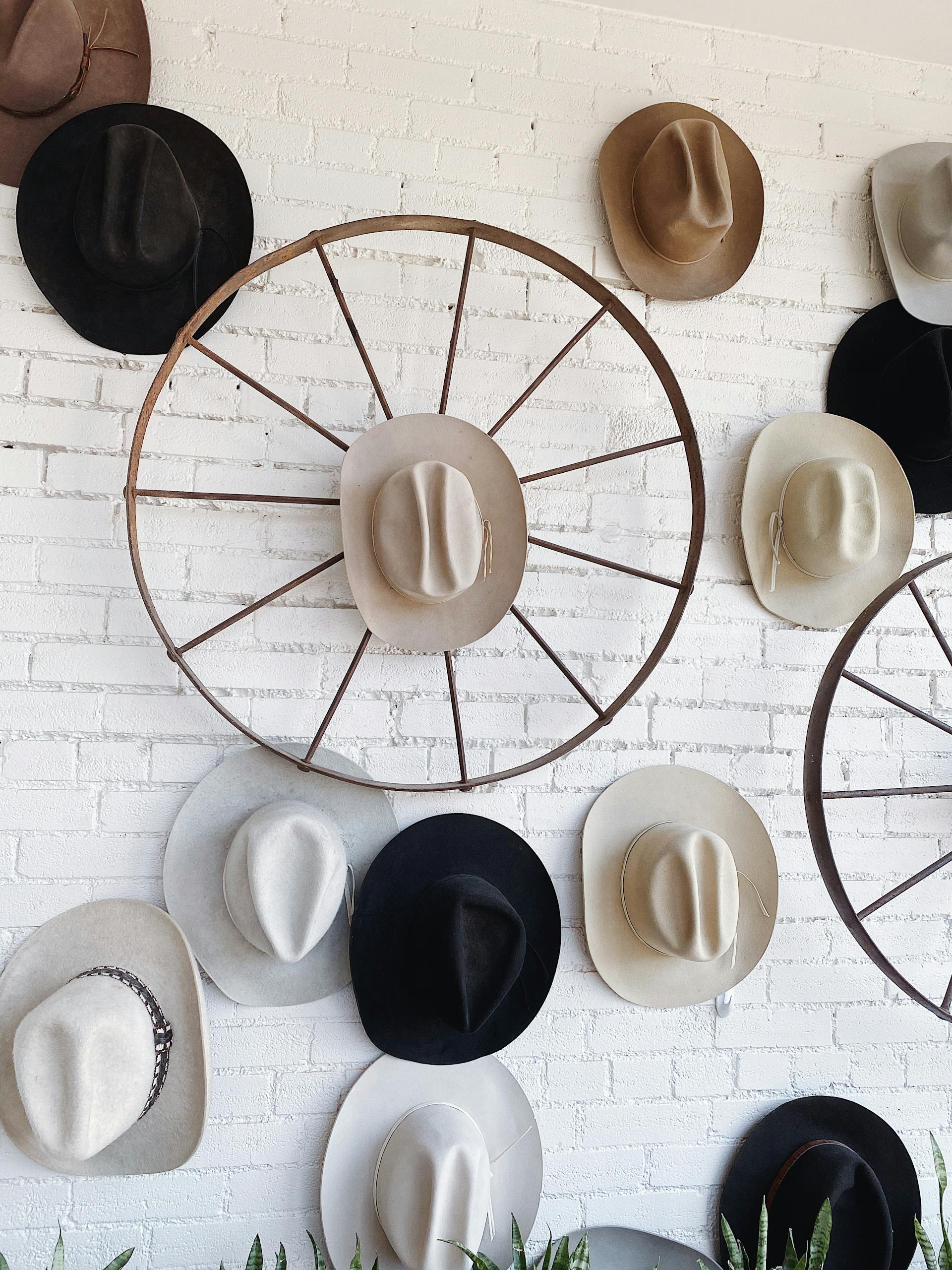 Decorative display of cowboy hats and wagon wheels on a rustic white brick wall indoors.